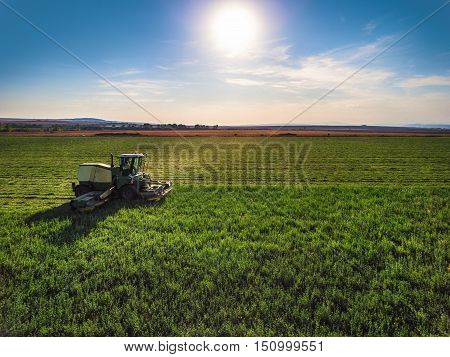Tractor mowing green field and bkue sky with clouds