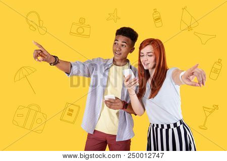 Lets Go There. Positive Active Friends Smiling And Holding Their Smartphones While Pointing To Diffe