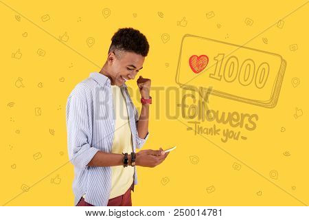 Popular Blogger. Cheerful Young Popular Blogger Looking At The Screen Of His Gadget And Celebrating 