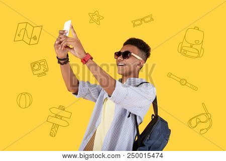 Taking Photos. Positive Young Man Wearing A Backpack And Smiling While Taking Photos During His Unfo