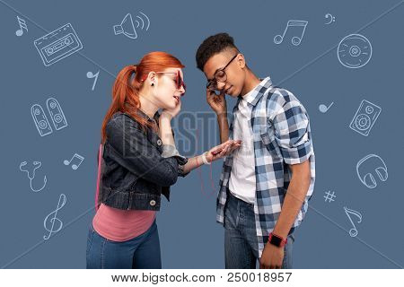New Earphones. Cute Young Girl Standing With A Modern Smartphone In Her Hands And Giving An Earphone