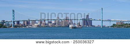 A Great Lakes Freighter Travels On The Detroit River Under The Ambassador Bridge Over Which A Steady