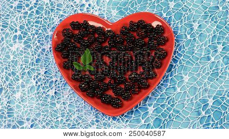 Organic Black Raspberry On A Decorative Red Plate In The Form Of A Heart. Blue Background. Top View.