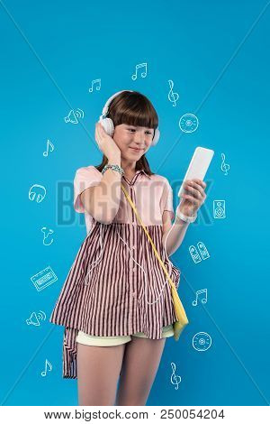 Pleasant Day. Cute Teenager Smiling And Feeling Glad While Listening To Music In Big Headphones