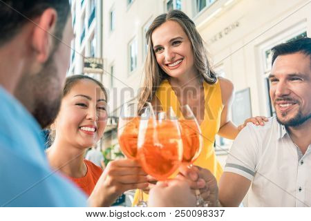Low-angle view of a multi-ethnic group of four friends celebrating together with an orange refreshing summer drink at a trendy restaurant downtown