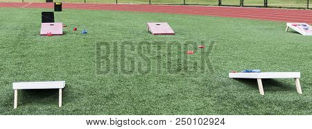 A High School Gym Class Has Wooden Corn Hole Games Set Up On Its Turf Field With Bean Bags For Class