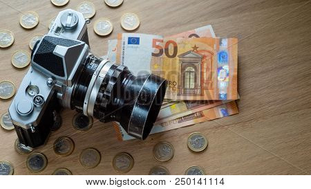 Euro Banknotes, Coins And A Camera On A Light Wooden Background.
