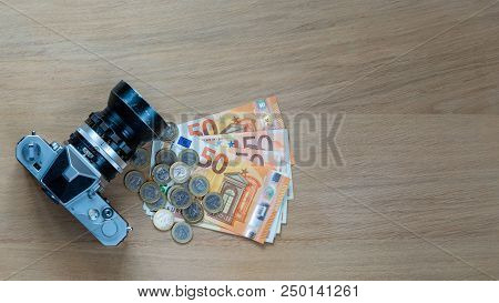 Euro Banknotes, Coins And A Camera On A Light Wooden Background.