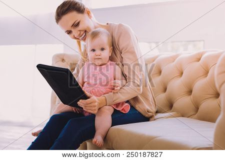 Progressive Babysitter. Lovely Baby Girl Sitting On The Knees Of A Babysitter And Looking At The Pic