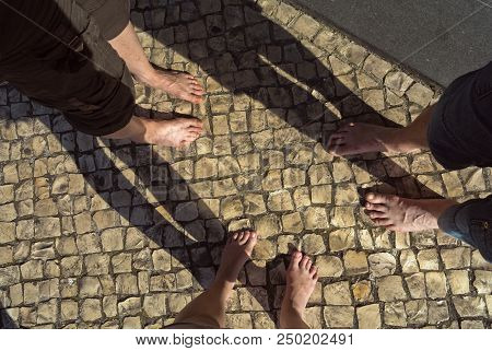 Three People With Naked Feet Are Standing In Cirkle On A Ground With Strong Shadows