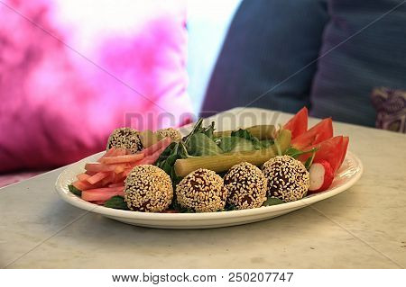 Falafel Balls Covered In Sesame In A Platter Along With The Traditional Accompanying Vegetables.