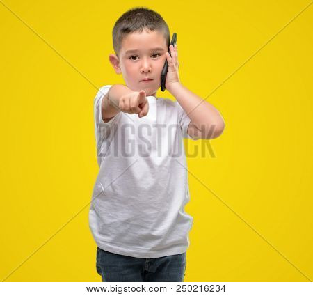 Dark haired little child using a smartphone pointing with finger to the camera and to you, hand sign, positive and confident gesture from the front