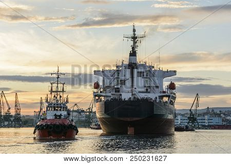 Tug Boat Entering The Harbor With Big Cargo Boat.