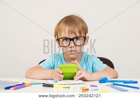 Little Boy In Glasses Sitting At Desk With School Supplies, Doing Homework At Table. Back To School.