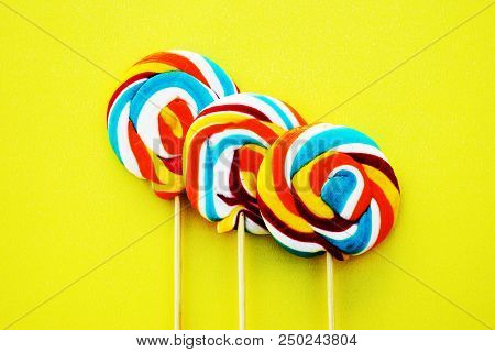 Colorful Hard Candy Lollipop On Yellow Pastel Background. Rainbow Sweet Pattern On Stick Flying Arou