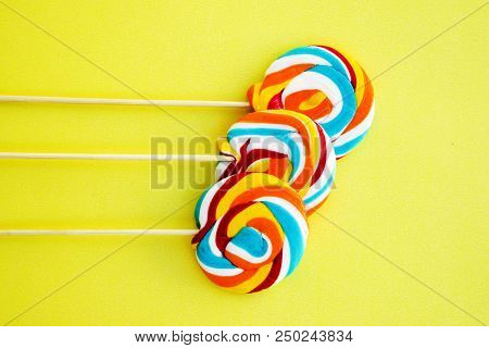 Colorful Hard Candy Lollipop On Yellow Pastel Background. Rainbow Sweet Pattern On Stick Flying Arou