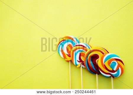 Colorful Hard Candy Lollipop On Yellow Pastel Background. Rainbow Sweet Pattern On Stick Flying Arou