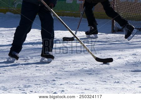 A Boy Ice Hockey Amateur Player With A Stick And A Puck On Ice. Feet In Hockey Skates And A Stick An