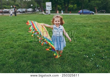 Laughing Little Cute Child Baby Girl In Denim Dress Running, Play With Colorful Kite And Have Fun In