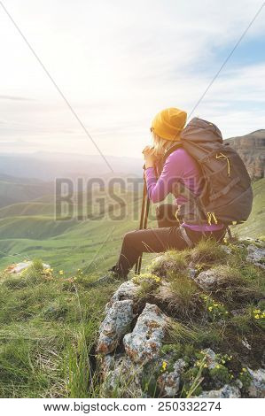 Smiling Girl Traveler In A Yellow Hat And A Pair Of Sunglasses Ssitting At The Foot Of Epic Rocks Wi
