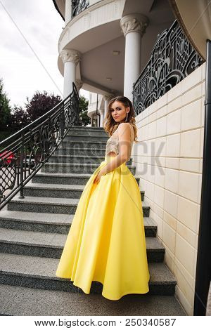 Lady In Yellow Erening Dress Stand On Stairs.