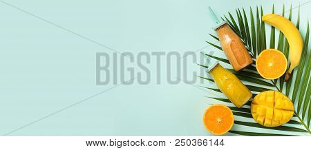 Exotic Orange, Banana, Pineapple, Mango Smoothie And Juicy Fruits On Palm Leaves Over Blue Backgroun