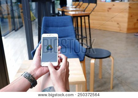 A Man Sit In Cafe Holding Mobile With Google Drive Screen