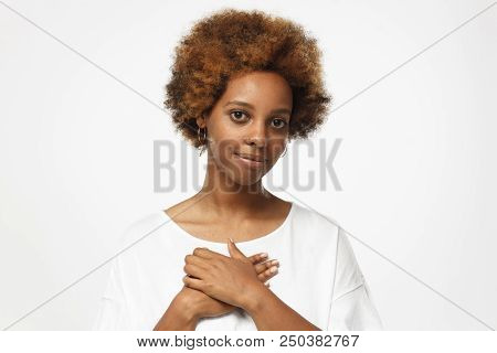 Portrait Of Smiling Young Woman Keeps Hands On Chest, Expresses Sympathy. Kind Hearted Friendly Afri