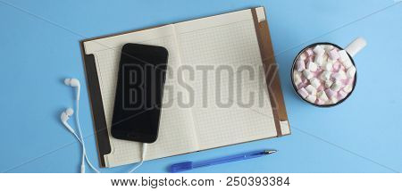 Work Space Mobile Phone, Notebook, Coffee Or Cocoa Drink  Marshmellow Blue Background