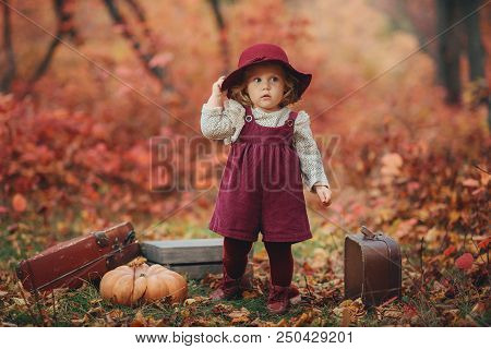 A Little Cute Girl In A Claret Hat And Dress Of Ancient Suitcase In Hands Stands Expectant In The Au