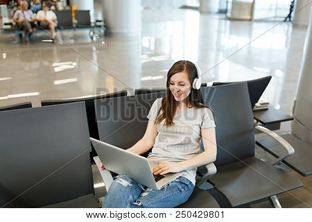 Young Calm Traveler Tourist Woman With Headphones Listening Music Working On Laptop, Waiting In Lobb