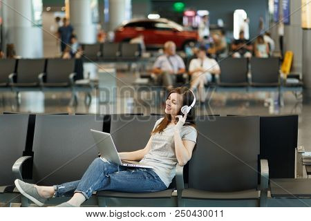 Young Relaxed Traveler Tourist Woman With Headphones Listening Music Working On Laptop, Wait In Lobb