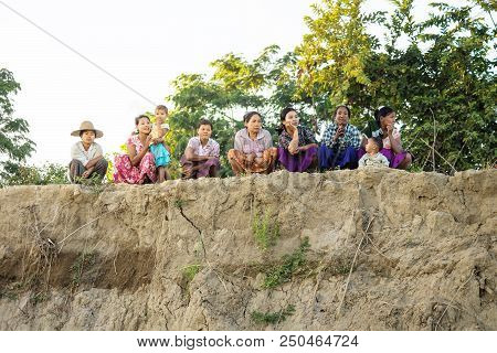 Irrawaddy River, Myanmar - December 26 2012: Women Sitting, Crouching And Watching On A Riverbank In