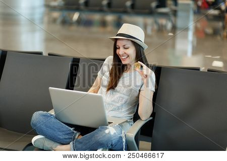 Young Smiling Traveler Tourist Woman In Hat Sit With Crossed Legs, Working On Laptop Holding Bitcoin