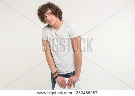 Handsome Young Man With Curly Hair Standing In White T-shirt Behind A Chair.