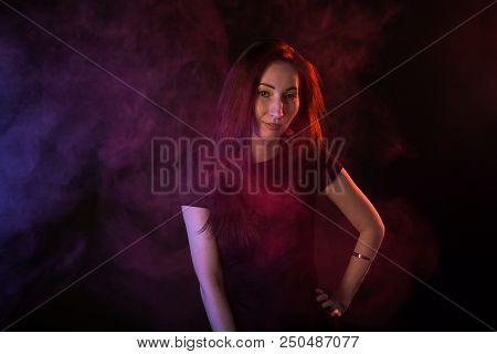 Young Woman In Neon Light And Smoke Of E-cigarettes Or Vape On Black Background.