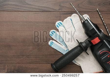 Hammer Drill And Working Gloves On The Wooden Background With Copy Space
