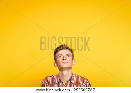 Serious Concentrated Handsome Man Looking Up. Portrait Of A Young Guy On Yellow Background Popping U
