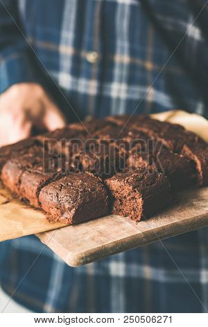 Vegan Chocolate Brownies With Dates And Nuts On Cutting Board. Hands Holding Tray Of Freshly Baked V