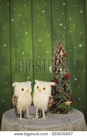 Two Christmas Owls On A Table Near A Decorative Christmas Tree On A Green Background. New Year Greet