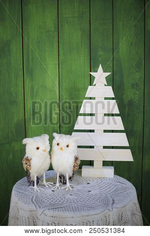 Two Christmas Owls On A Table Near A Decorative Christmas Tree On A Green Background. New Year Greet