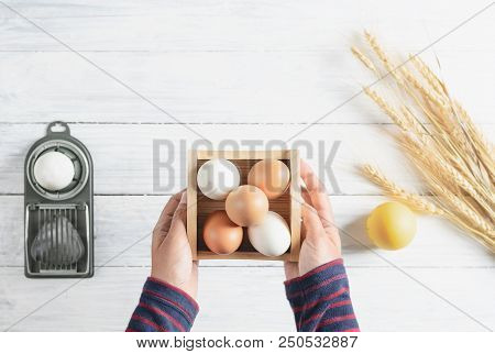 Top View Hands Holding Chicken Egg In Box, White Wood Background