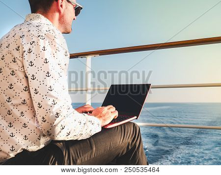 Stylish, Attractive Man With Laptop On The Deck Of A Cruise Ship On A Background Of Sea Waves And Bl