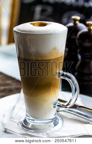 Hot Latte Macchiato Coffee With Tasty Foam And Cinnamon In Tall Clear Glass On Serving Table