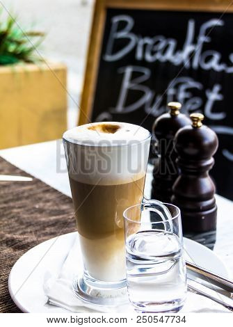 Hot Latte Macchiato Coffee With Tasty Foam And Cinnamon In Tall Clear Glass On Serving Table