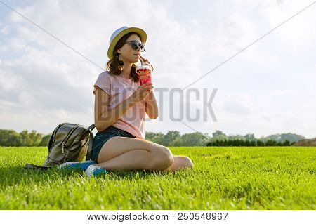 Young Girl In Sunglasses And Hat Drinks Summer Berry Drink With Ice Sitting On Green Grass. Copy Spa
