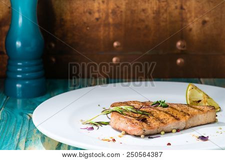 Close-up Tasty Cooked Steak On A White Plate With Lemon And Herbs, On A Wooden Table. Brown Backgrou