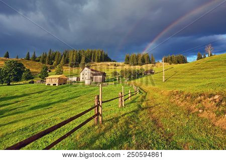A Farm House In A Green Sunny Field And A Rainbow.