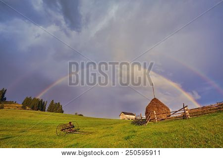 A Farm House In A Green Sunny Field And A Rainbow.