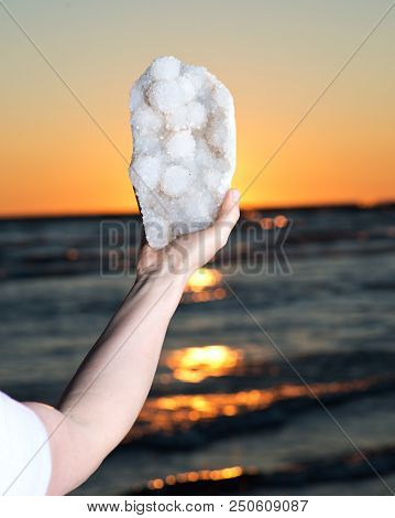 Woman Holding Aurora Rainbow Quartz Cluster From India  In Her Hand At Sunrise In Front Of The Lake.